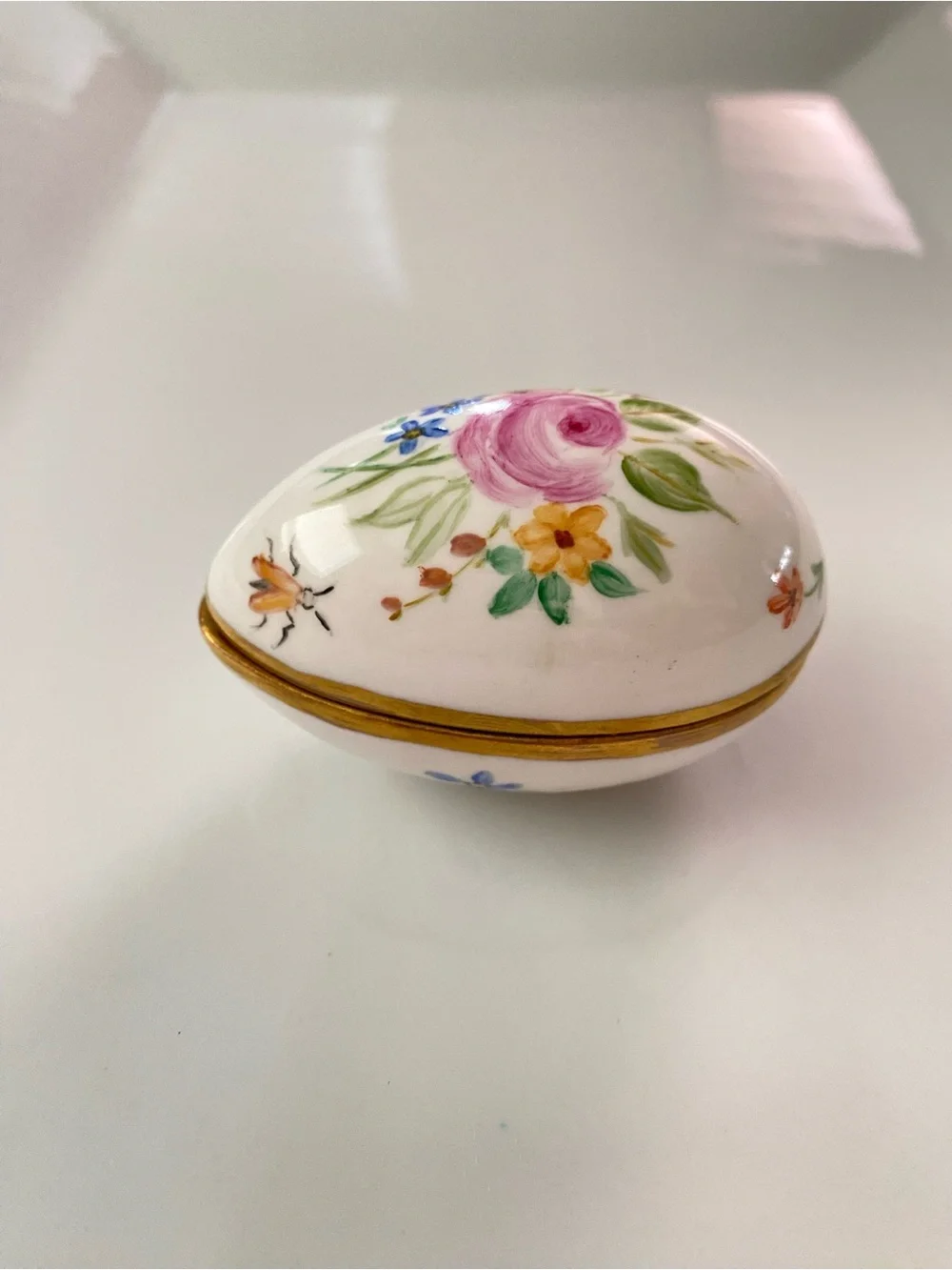 A hand-painted and signed porcelain egg-shaped trinket box with gilded trim.